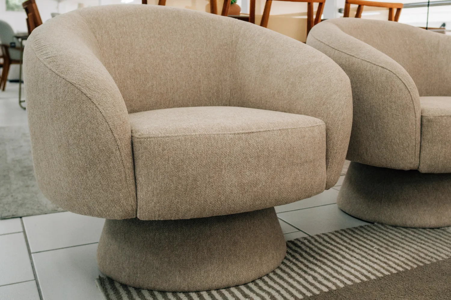 Par de poltronas giratórias em bouclé bege, com base arredondada, no showroom da JEB